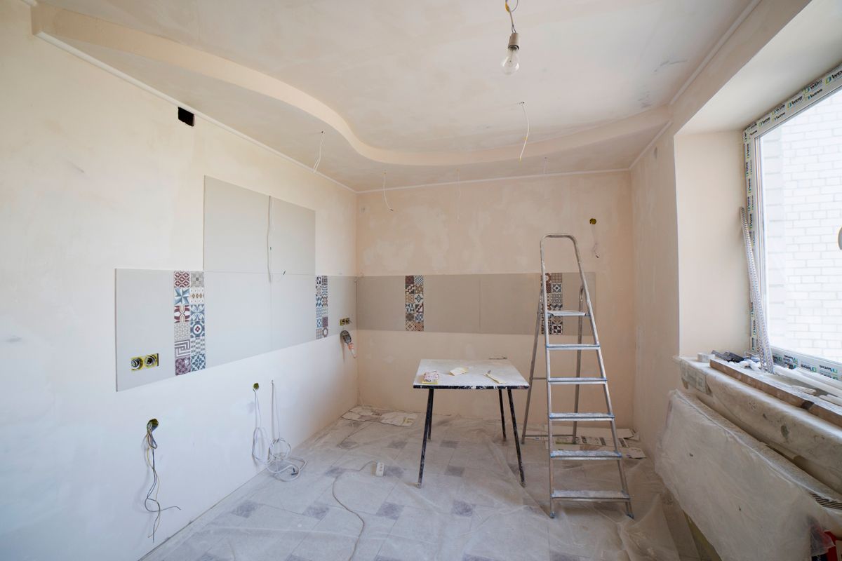 Kitchen mid-renovation with a stepladder, dust sheets on the floor, and a freshly plastered curved ceiling soffit